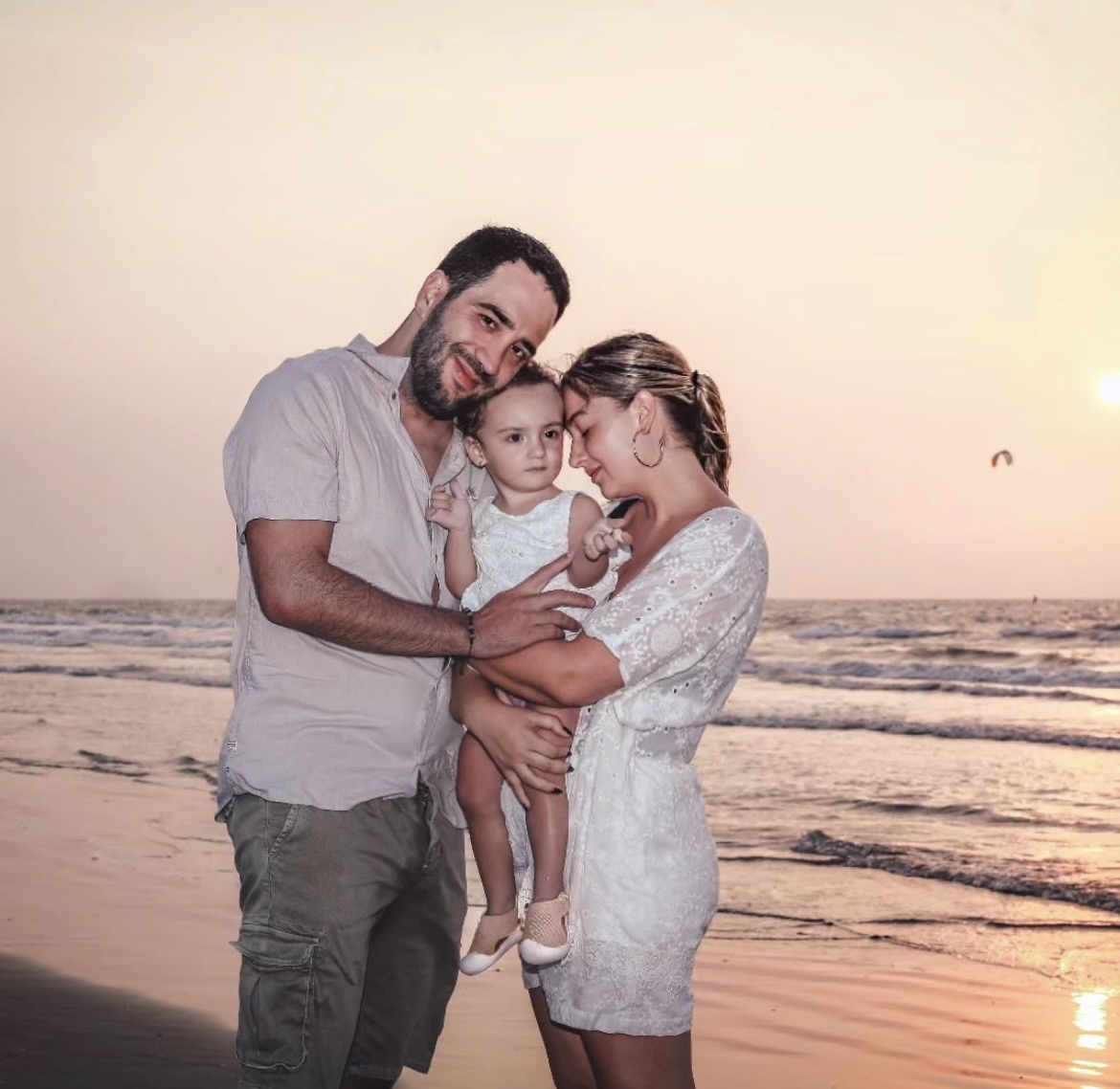 Adelaida, su esposo y su bebé abrazados en la playa al atardecer